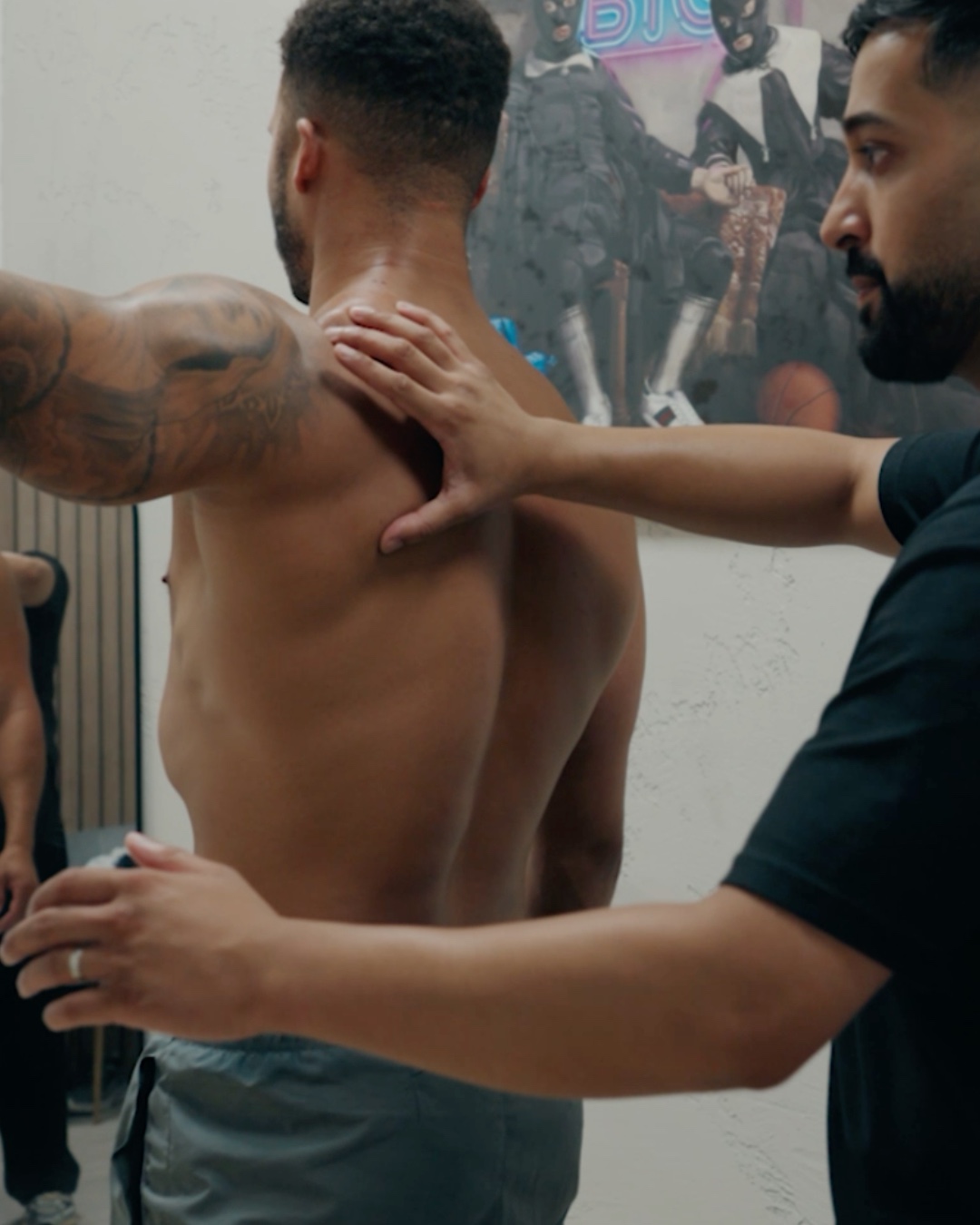 Standing, one hand at the neck and one at the low back, reading how the body is holding itself.
